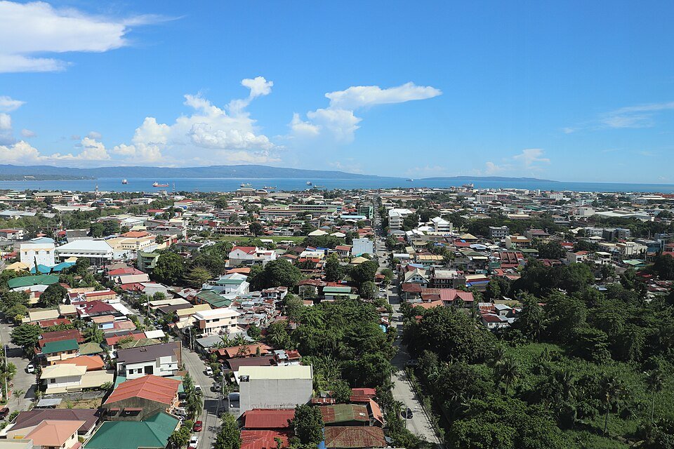 Panoramic view of Davao City, with residential neighbourhoods, greenery and Davao Gulf in the background.