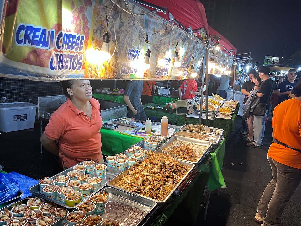 Food stall at Davao's Roxas Night Market displaying prepared dishes beneath illuminated market tents.