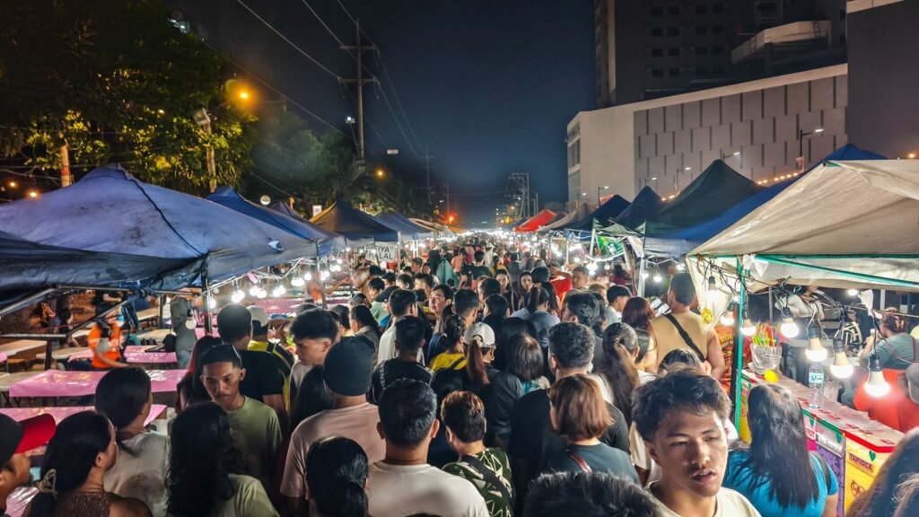 Crowds of visitors exploring illuminated food stalls at Roxas Night Market in Davao City at night.