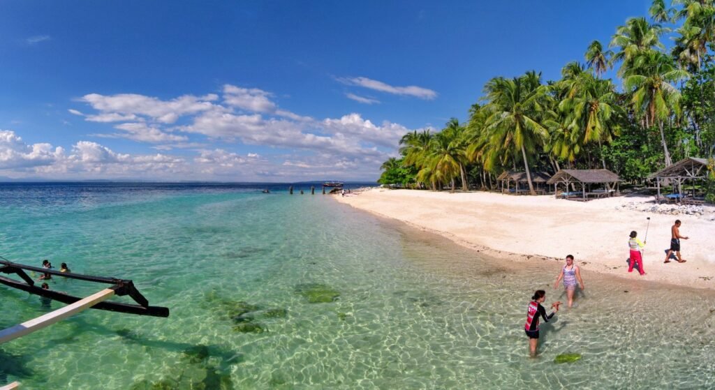 White sandy beach on Samal Island with clear turquoise water, coconut palms and visitors enjoying the shoreline.