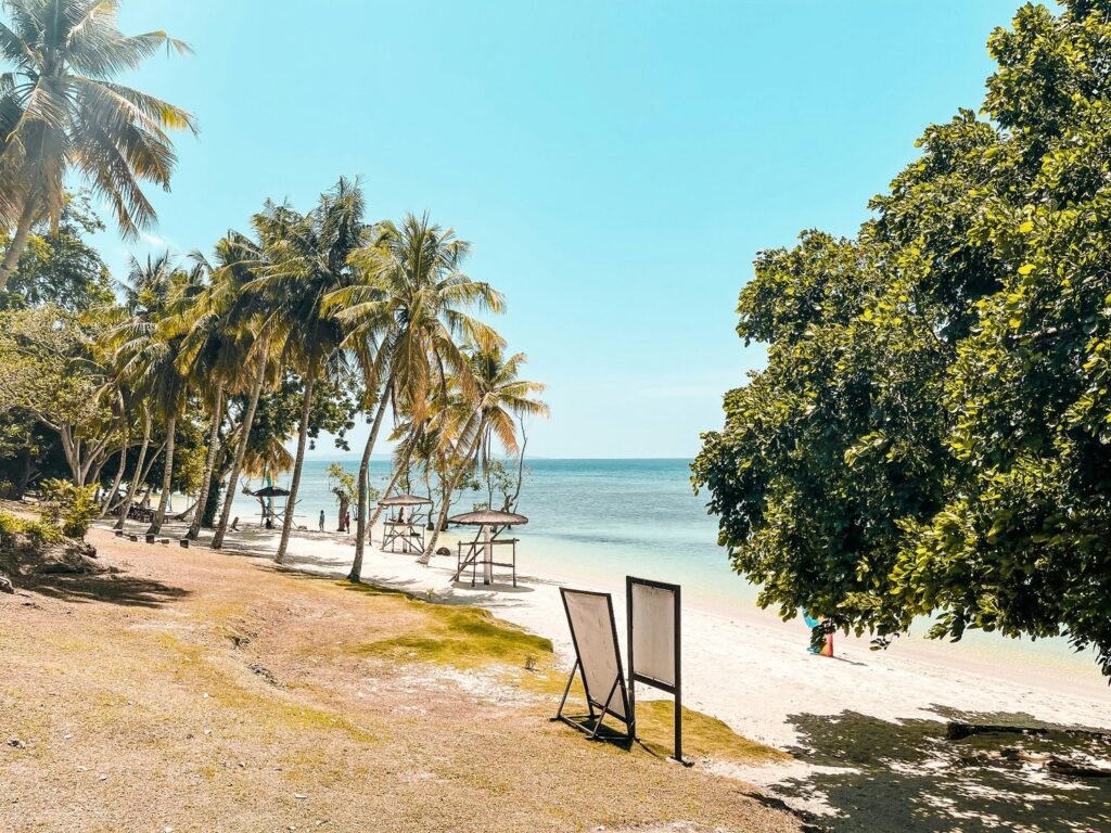 Sunny beach on Samal Island, Philippines, with coconut palms, white sand, clear blue water and shaded seating areas.