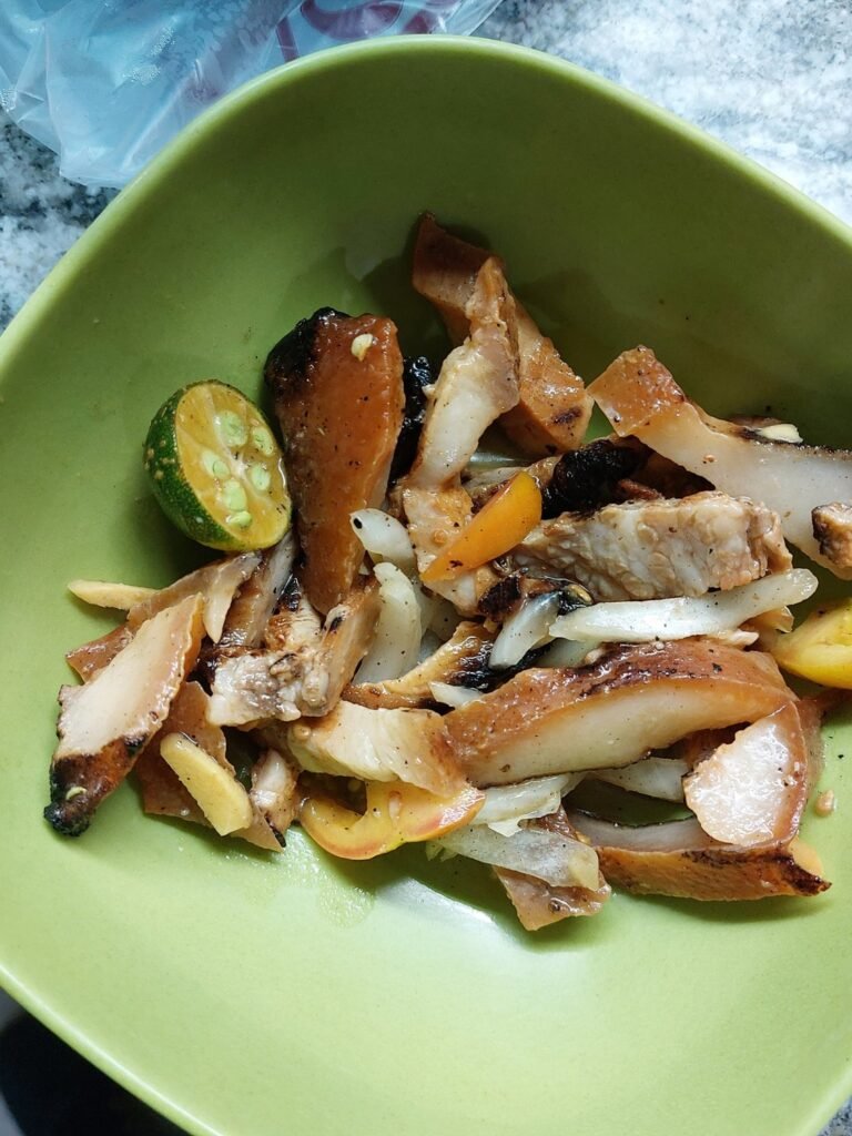 Filipino sinuglaw dish with grilled pork, onions and calamansi served in a green bowl.